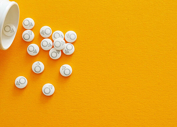 Testosteron-Ersatztherapie hilft nicht bei sexueller Dysfunktion, es steigert nicht die Potenz. Eine offene Tablettendose, aus der Tabletten herauskullern: Sie sind mit dem Männlichkeitssymbol geprägt (Kriegsgott Mars, Kreis und Pfeil).