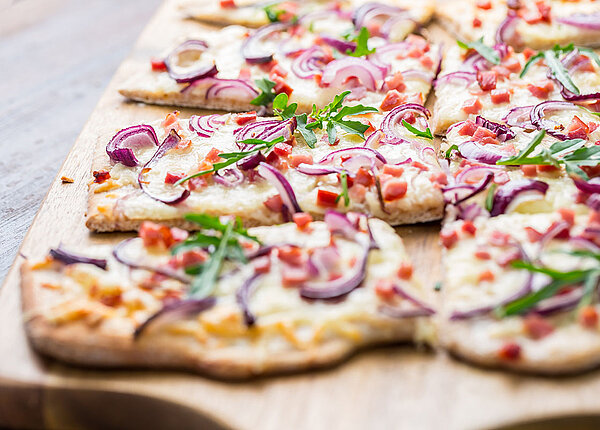 Flammkuchen selber machen Nahaufnahme eines klassischen Flammkuchens auf Holzbrett