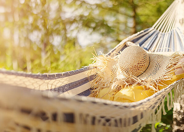 Verantwortung auch mal abgeben und entspannen Frau in Hängematte. Ihr Gesicht ist mit einem Strohut bedeckt.