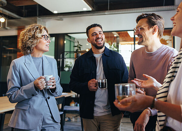 Mehr Erfolg im Job dank Small Talk Vier Kolleg*innen unterhalten sich und haben einen Kaffee oder Tee in der Hand.