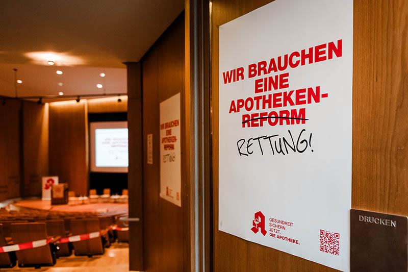 An der Tür zum Podiumssaal hängt ein Schild: Ursprünglich stand dort: „Wir brauchen eine Apothekenreform.“ „Reform“ ist durchgestrichen, stattdessen wure dort „Rettung“ hingeschrieben.