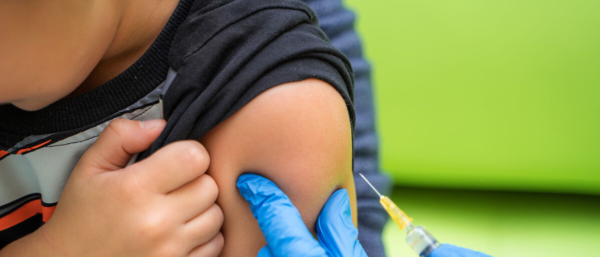 Kleiner Junge mit blauem T-Shirt bekommt eine Impfung. Der Arzt hat blaue Handschuhe an