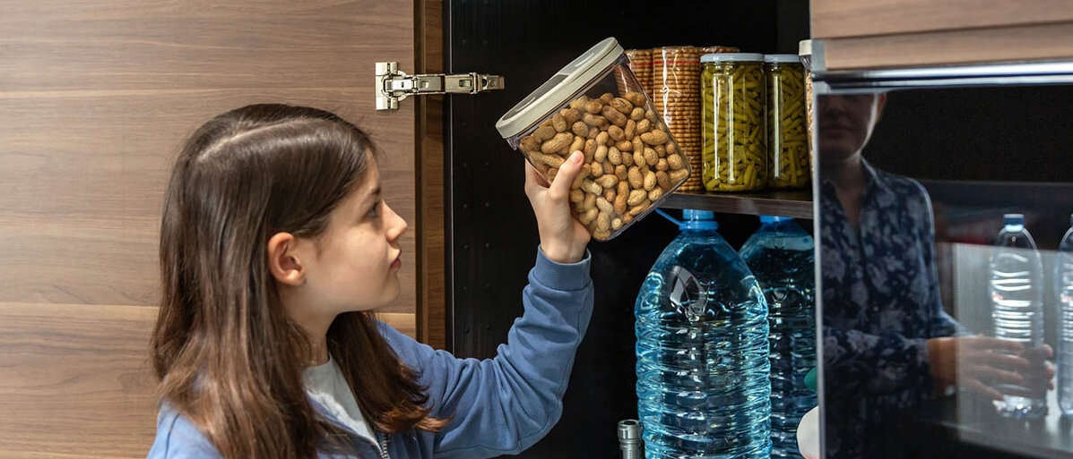 Erdnussallergie bei Kindern: neue Studie zur Desensibilisierung Ein Mädchen stellt ein Vorratsglas mit Erdnüssen in den Schrank.