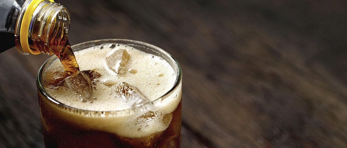 Cola wird in ein Glas mit Eiswürfeln eingegossen.