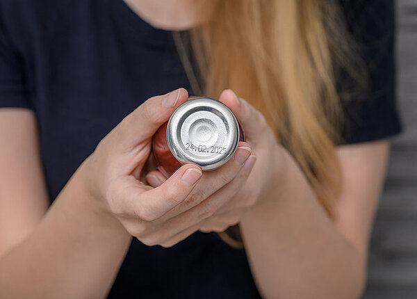 Mindesthaltbarkeitsdatum abgelaufen Frau prüft Flasche mit Tomatensoße, auf deren Deckel man ein Mindesthaltbarkeitsdatum erkennt.