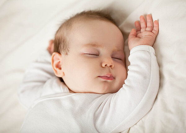Ein Baby schläft auf dem Rücken, den Kopf nach links gedreht.