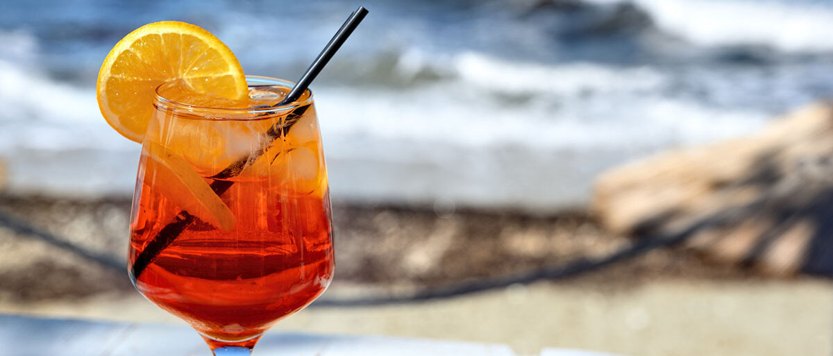 Ein Glas mit Aperol Spritz, garniert mit Orangenscheibe und Trinkhalm