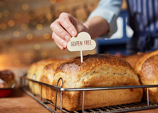 In einer Bäckerei wird ein Holz-Spicker mit der Aufschrift „Gluten Free“ in einen Laib Brot gesteckt.