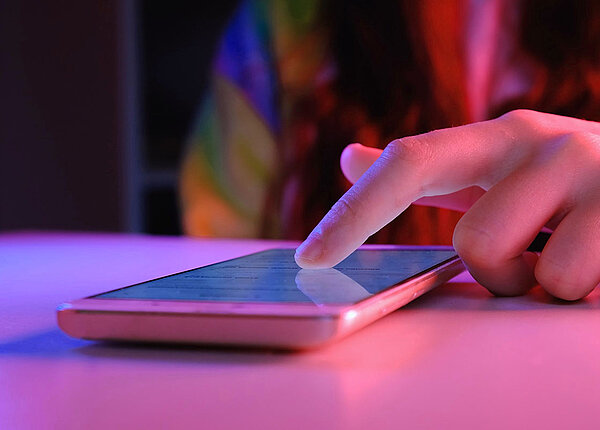 Smartphone mit rosa Hülle liegt auf einem Tisch und ein Finger liegt auf dem Display.