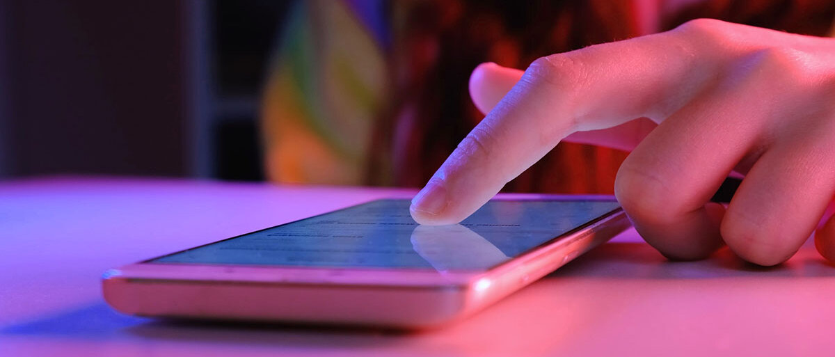 Smartphone mit rosa Hülle liegt auf einem Tisch und ein Finger liegt auf dem Display.