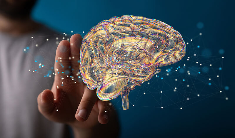 Jemand zeigt auf die Illustration eines Gehirns, das im Raum schwebt. Um das Gehirn herum sind Verbindungen angedeutet sowie leuchtende Punkte.