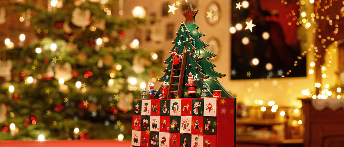 Adventskalender und im Hintergrund steht ein stilisierter Weihnachtsbaum inmitten von bunter Weihnachtsdeko.