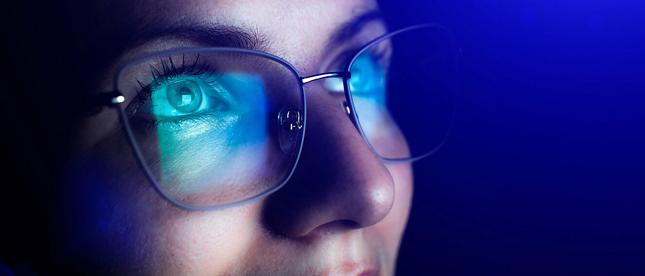Nahaufnahme des oberen Teils des Gesichts einer Frau, die eine Brille trägt. In den Gläsern spiegelt sich ein Bildschirm.