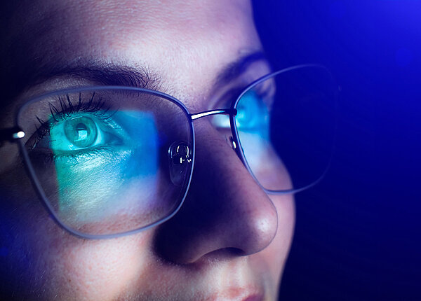 Nahaufnahme des oberen Teils des Gesichts einer Frau, die eine Brille trägt. In den Gläsern spiegelt sich ein Bildschirm.