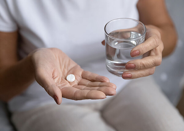 In einer Frauenhand liegt eine weiße Tablette und die andere Hand hält ein Wasserglas.