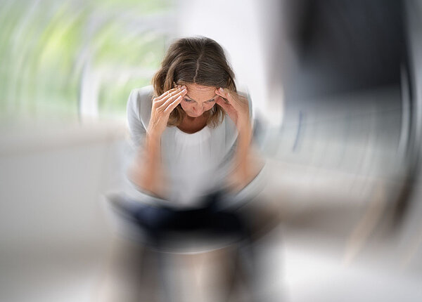 Sitzende Frau mit dunklen Haaren hat ihre Hände an den Schläfen und um se herum dreht sich alles.