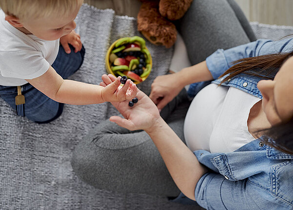 Schwangere Mutter und Sohn reichen einander Beeren