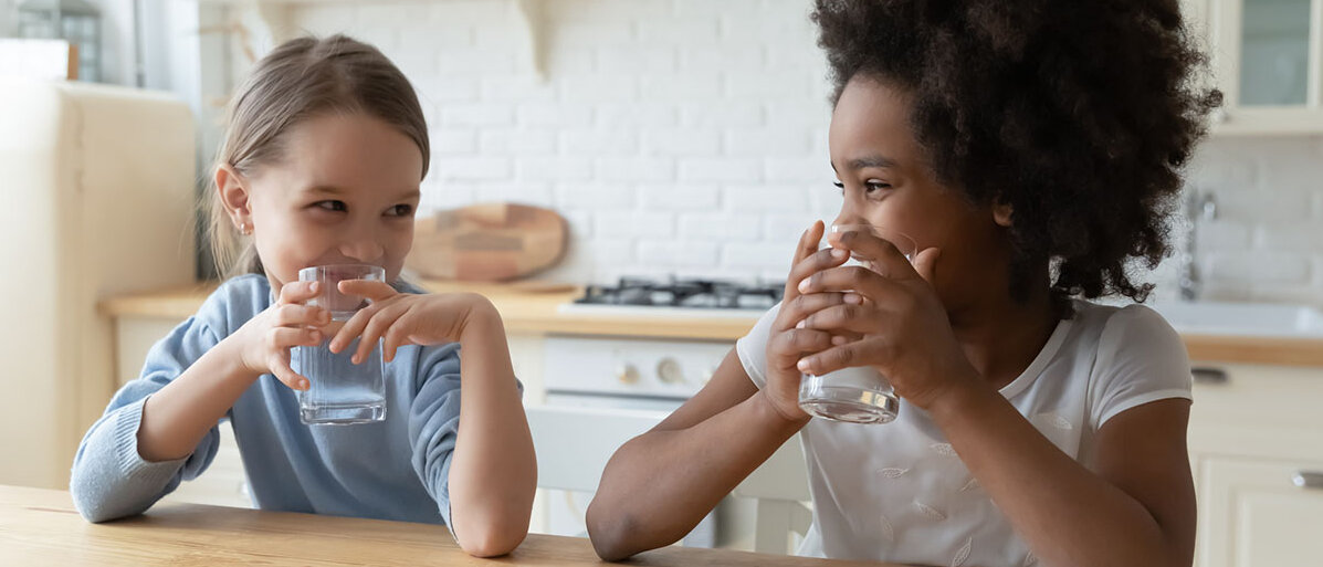 Afroamerikanische und kaukasische Mädchen trinken Wasser in der Küche