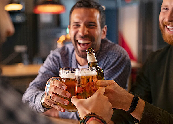 Drei Männer prosten sich mit Bier zu und lachen.