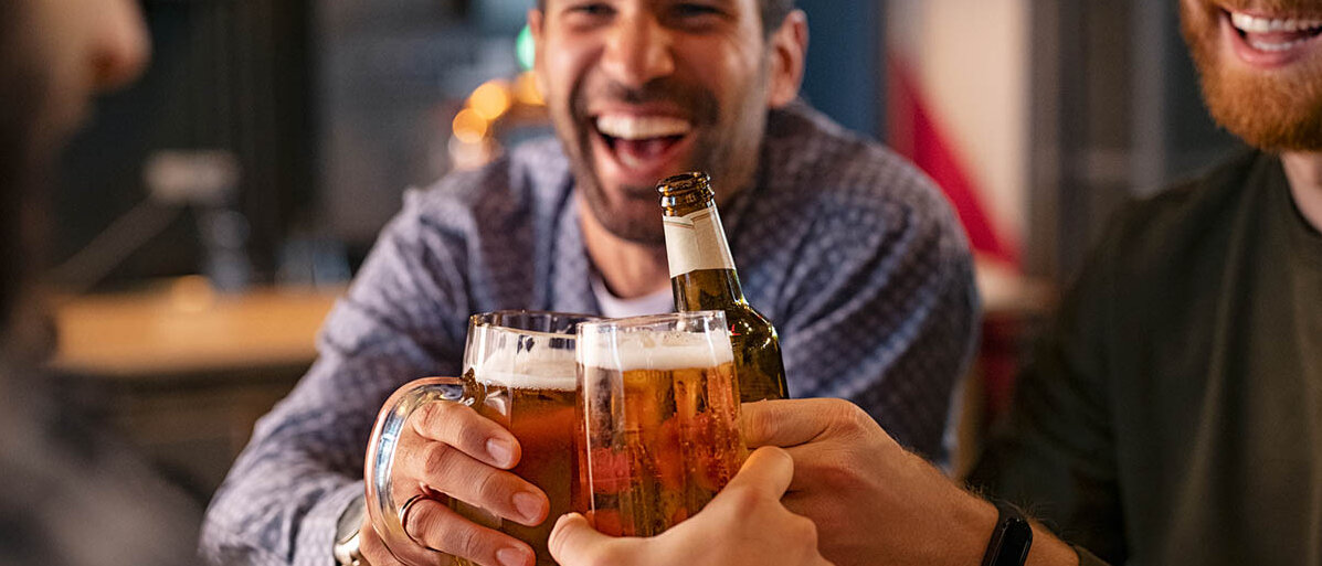 Drei Männer prosten sich mit Bier zu und lachen.