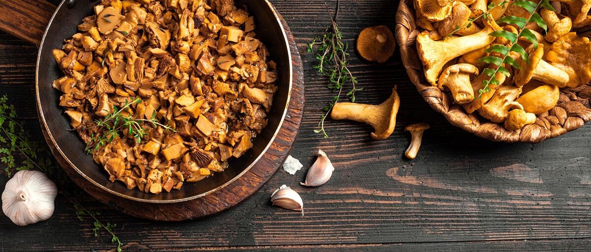 Eine Pfanne und ein Körbchen mit frischen Pfifferlingen auf einem dunklen Holztisch 