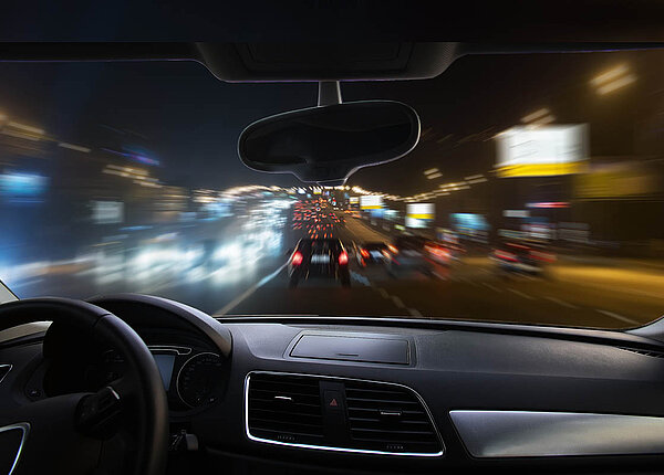 Blick durch die Windschutzscheibe eines Autos auf die Autobahn bei Nacht: Die Sicht ist verschwommen, die Lichter der anderen Autos blenden.