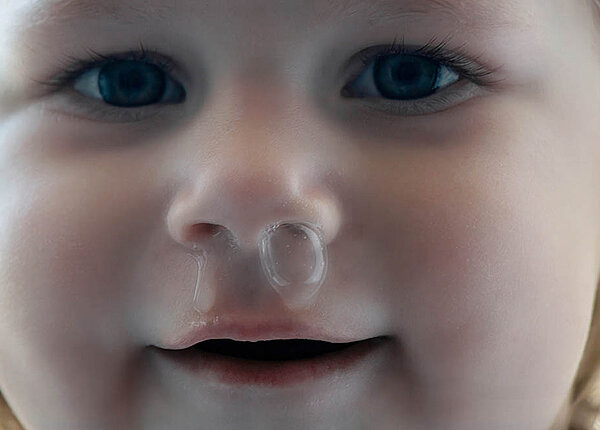 Kind krank durch Kita: Warum Kleinkinder viele Infekte durchmachen Einem Kleinkind blubbert Schnupfen aus der Nase.