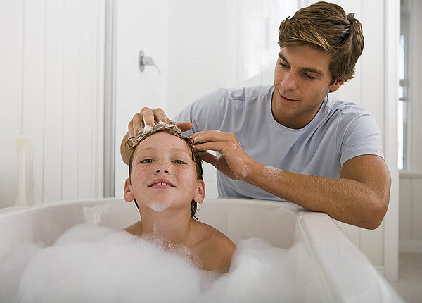 Ein Vater wäscht seinem Sohn in der Badewanne die Haare.