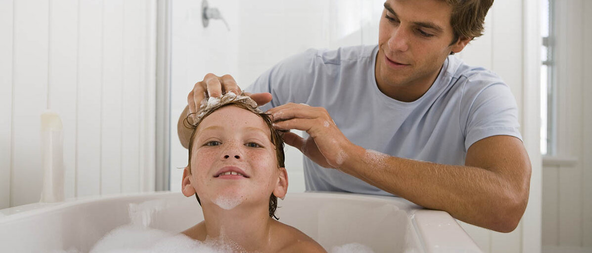 Ein Vater wäscht seinem Sohn in der Badewanne die Haare.