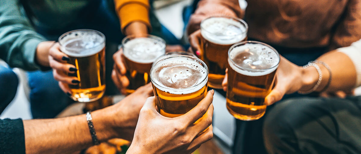 Gruppe von Menschen stößt mit Bier an. Fünf Biergläser sind zu sehen