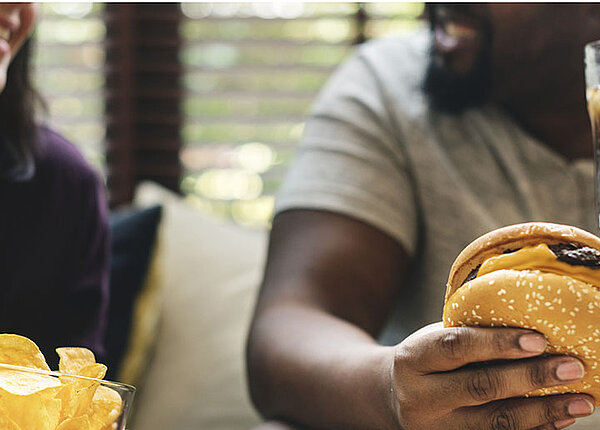 Partnerwahl und Ernährung Paar isst Burger und Chips auf der Couch