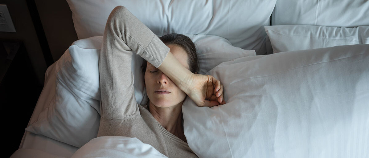 Frau liegt im Bett, hat eine Hand auf ihrem Gesicht und kann nicht schlafen