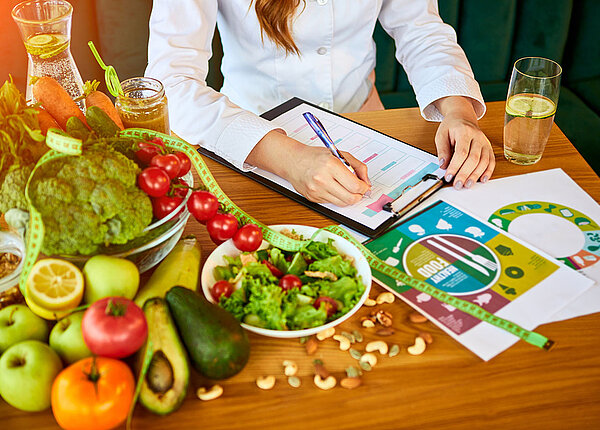 Frau sitzt an Tisch mit pflanzlichen Lebensmitteln und erstellt einen Ernährungsplan