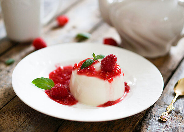 So gelingt eine Panna Cotta Panna Cotta mit Himbeersauce und Minze auf einem weißen Teller