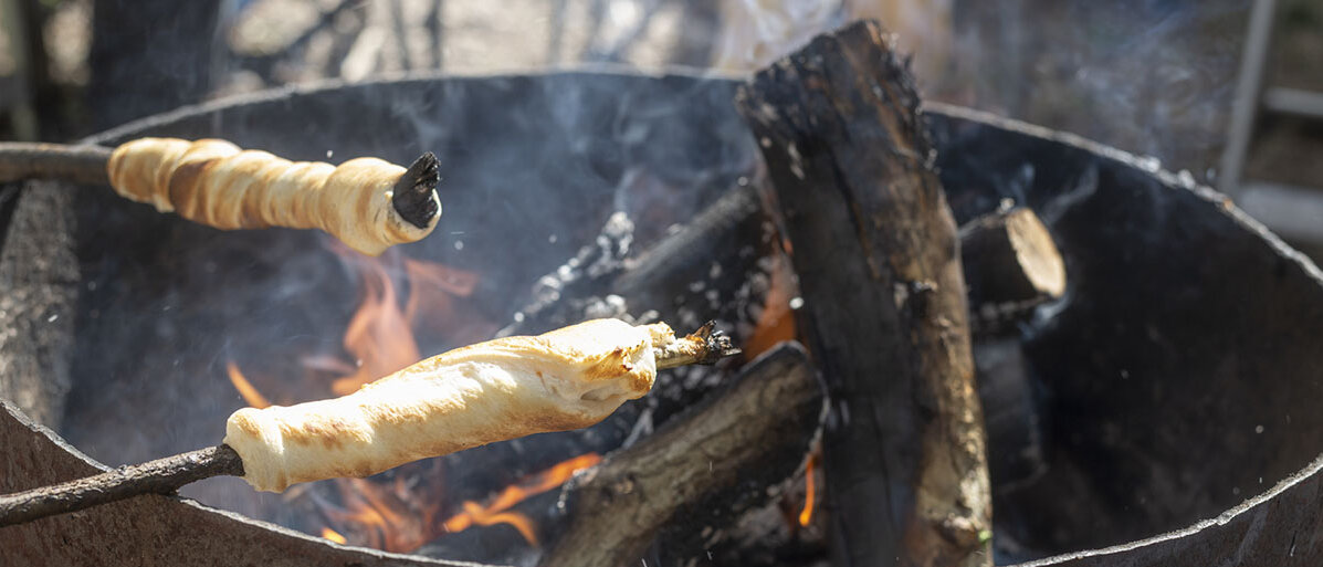 Grillschale und zwei Stöcke mit Teig drum gewickelt hängen über der Glut