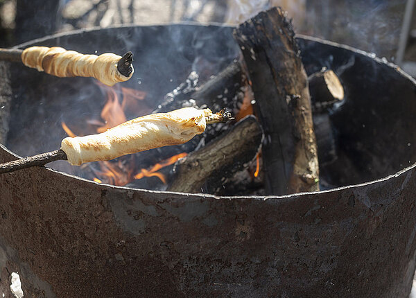 Grillschale und zwei Stöcke mit Teig drum gewickelt hängen über der Glut