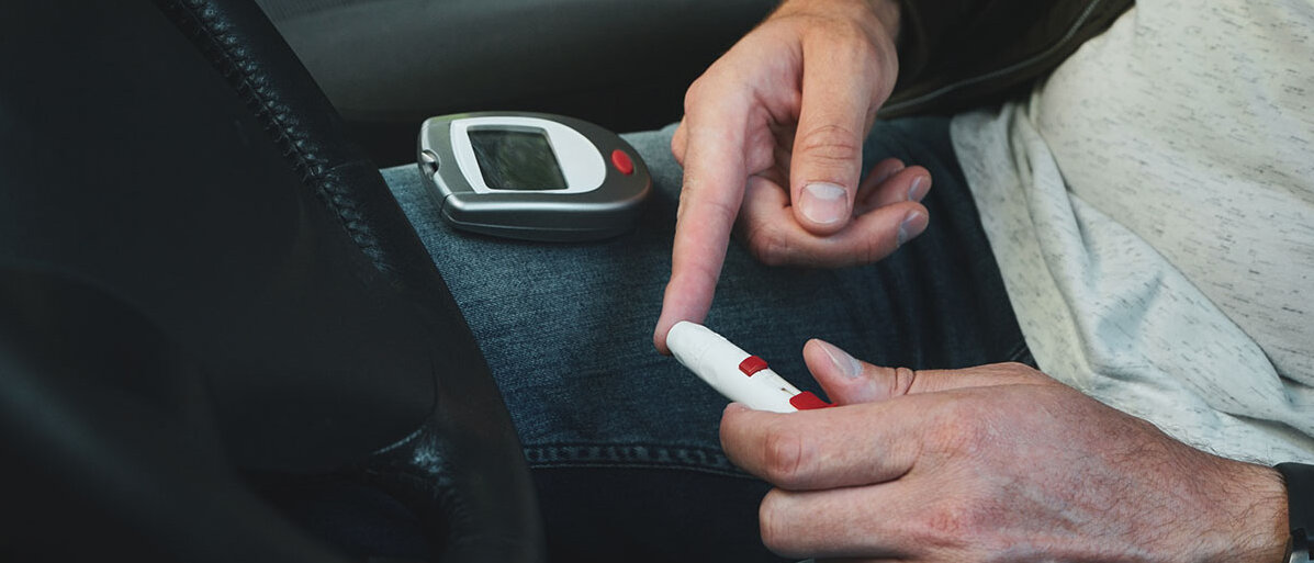 Sicher unterwegs mit Diabetes und Autofahren Mann sitzt in seinem Auto und misst mit einem Pen seinen Blutzuckerspiegel