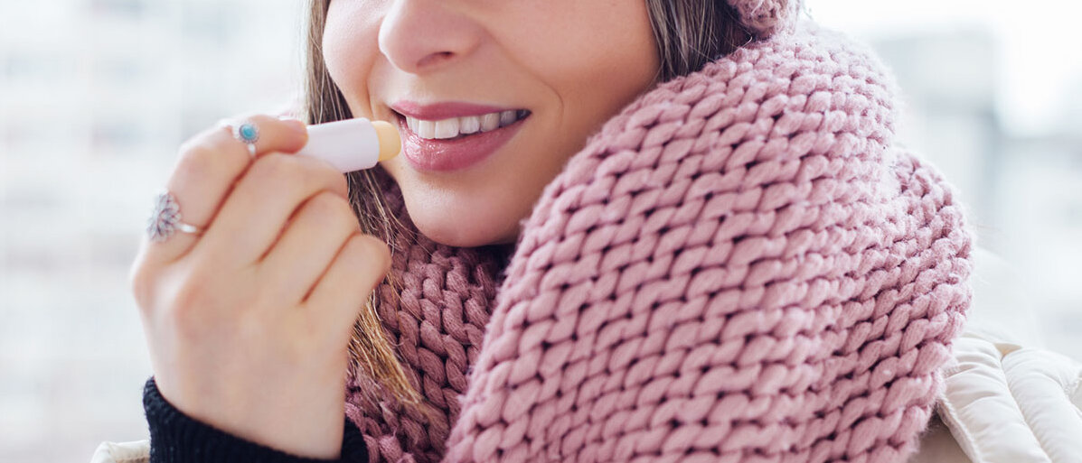 Junge Frau in Winterjacke und Schal trägt Lippenbalsam auf