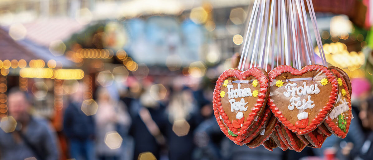 Weihnachtsmarkt mit Besuchern und im Vordergrund ist ein Stand mit Lebkuchenherzen zu sehen.