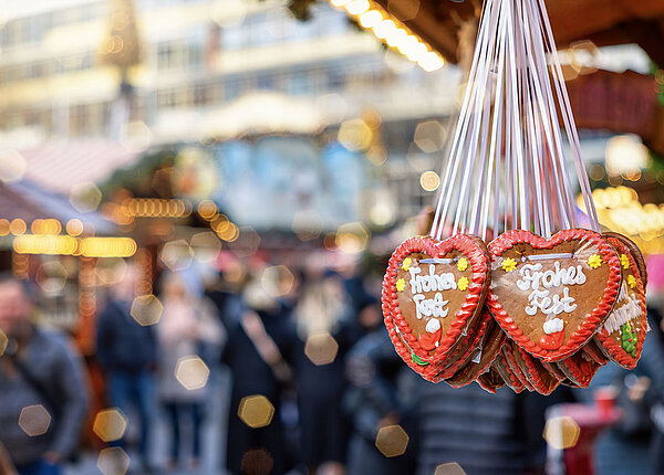 Weihnachtsmarkt mit Besuchern und im Vordergrund ist ein Stand mit Lebkuchenherzen zu sehen.