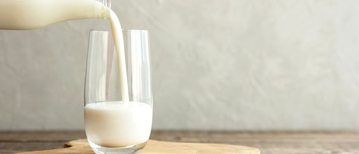 Glas Milch steht auf einem Holzbrett und auch einer Flasche mit Milch wird gerade Milch eingeschenkt.