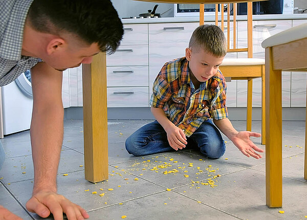 Dyspraxie bei Kindern: Symptome einer Entwicklungsstörung der motorischen Funktionen Vater und Sohn unter dem Küchentisch: Der Sohn hat Cornflakes verschüttet. Beide räumen gemeinsam auf.
