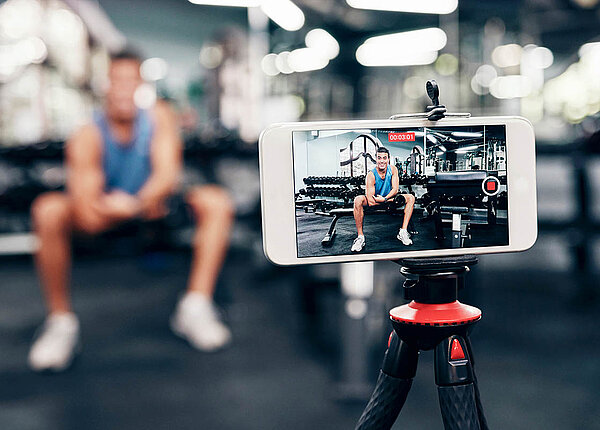 Peptide als Spritze: Das ist die Wirkung und diese Risiken drohen. Ein muskulöser Mann im Fitnessstudio filmt sich dabei, wie er auf seinen Bizeps zeigt.