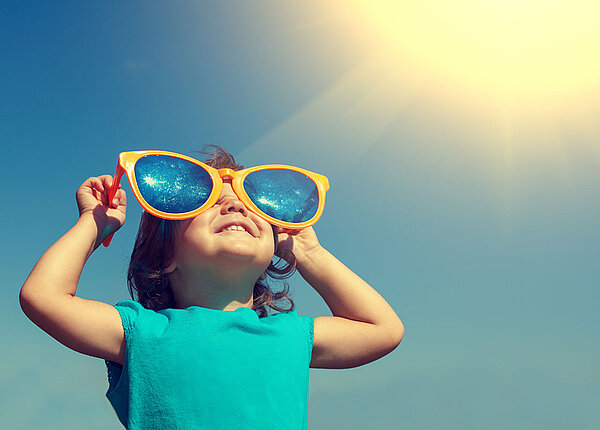 glückliches Kind schaut mit einer übergroßen Sonnenbrille in die Sonne