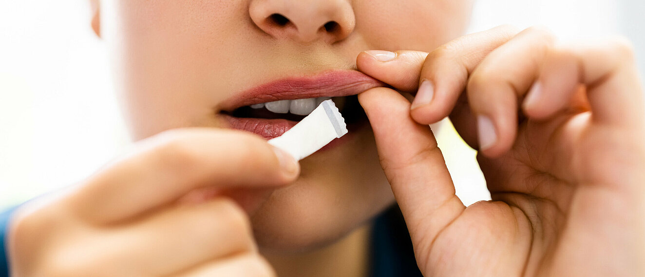 Eine Frau zieht mit der linken Hand ihre Oberlippe etwas nach vorne und schiebt mit der rechten Hand ein weißes Snus zwischen Lippe und Zahnfleisch.