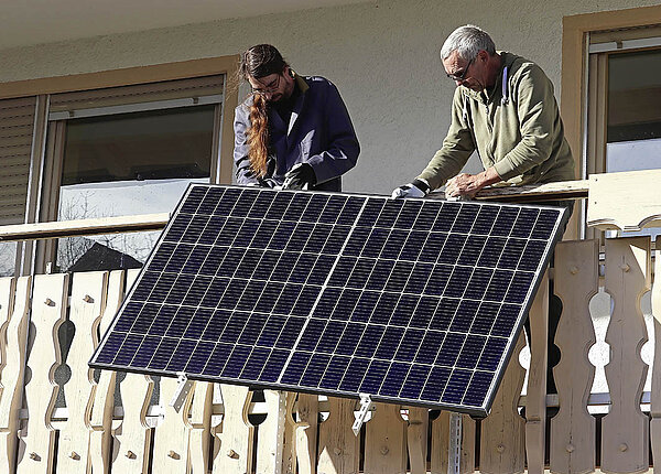 Zwei Männer montieren ein Photovoltaik-Modul an einem Balkon