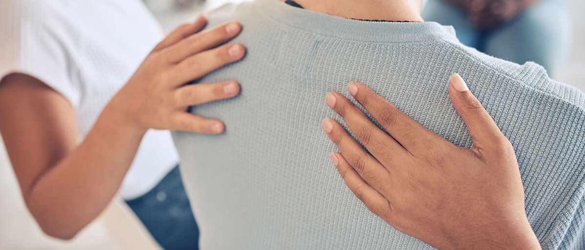 Zwei Frauen legen tröstend die Hand auf den Rücken einer weiteren Frau