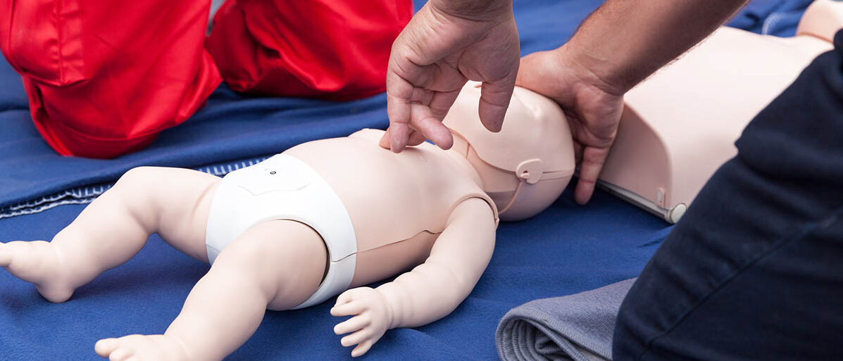 Zwei Personen in Rettungsdienst-Bekleidung üben eine Herzdruckmassage an einer Puppe in Größe eines Säuglings.