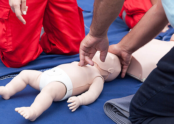 Zwei Personen in Rettungsdienst-Bekleidung üben eine Herzdruckmassage an einer Puppe in Größe eines Säuglings.