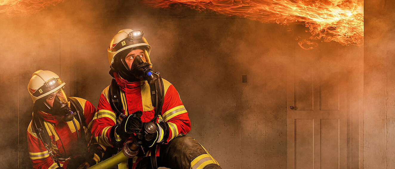 Zwei Feuerwehrmänner löschen Feuer an der Decke im inneren eines Hauses